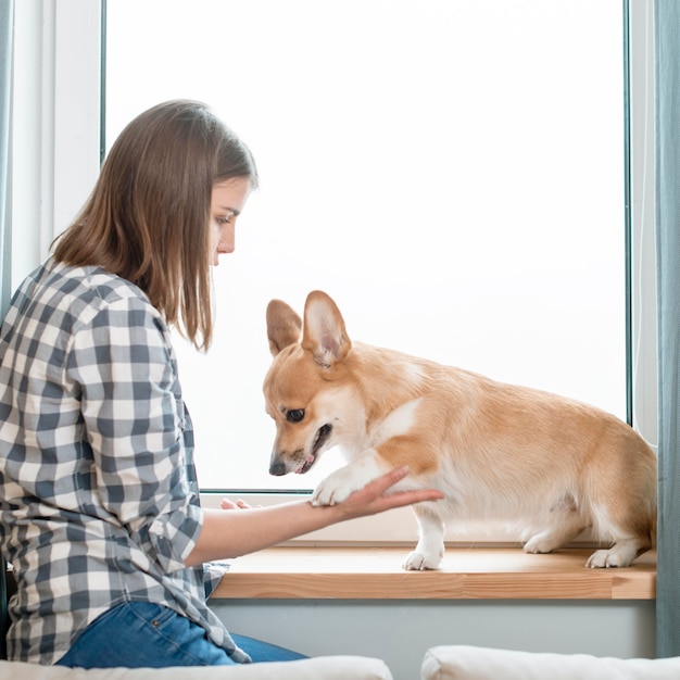 Free photo side view of woman and dog in front of window