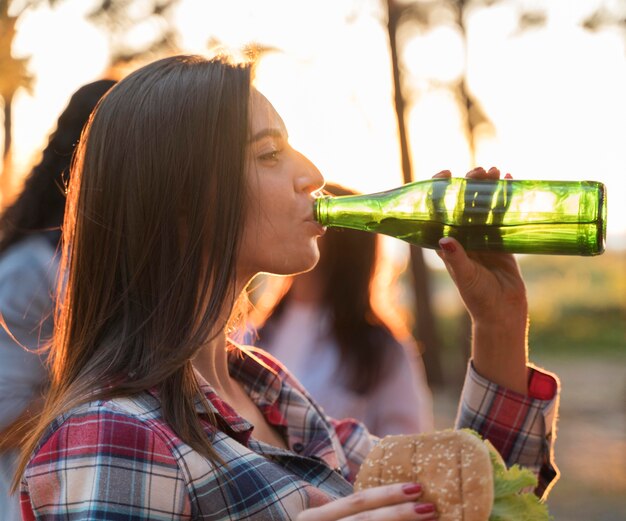 Side view of woman drinking beer outdoors with friends