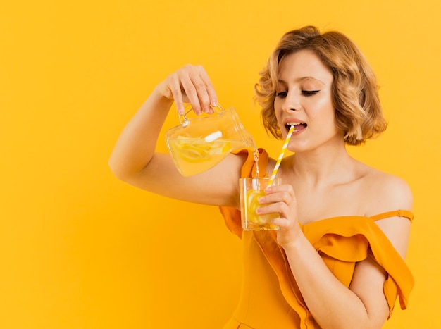 Side view woman drinking and pouring lemonade