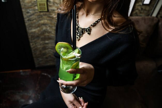 Side view woman drinking refreshing cocktail from kiwi