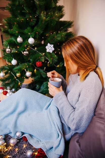 Side view of woman drinking tea next to christmas tree