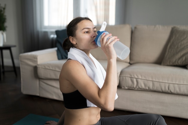 Free photo side view of woman drinking water after exercising