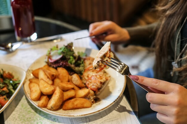 Side view woman eating fried chicken with potatoes