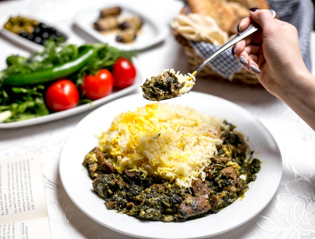 Vista laterale di una donna che mangia un piatto tradizionale azero shabzi pilaf carne fritta con verdure e riso bollito con verdure ed erbe