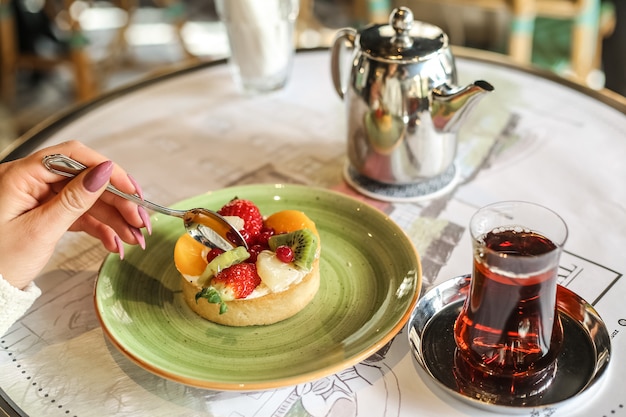 Side view woman eats fruit dessert with a glass of tea