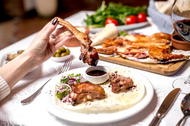 Vista laterale una donna mangia costolette di agnello kebab con salsa e cipolle