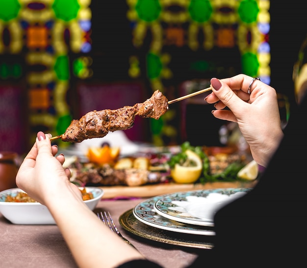 Side view woman eats kebab meat on a skewer