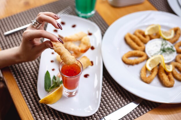 Side view woman eats shrimps in batter with sweet chili sauce and a slice of lemon