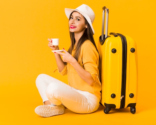 Side view of woman enjoying her cup of coffee next to luggage