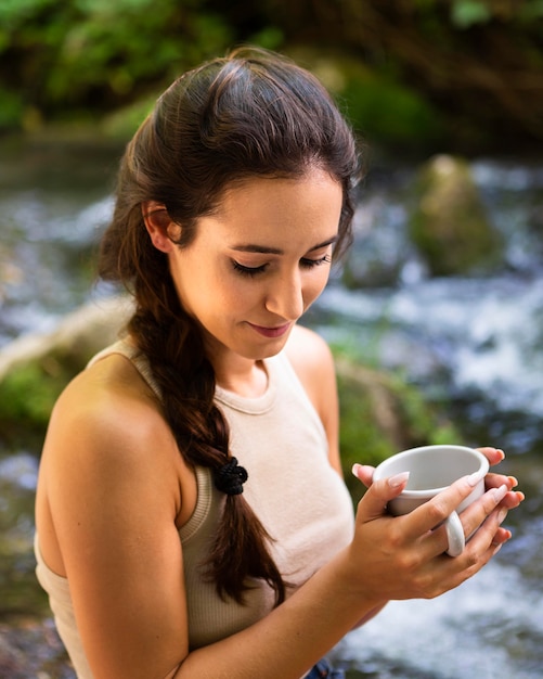 Side view of woman exploring nature and drinking coffee