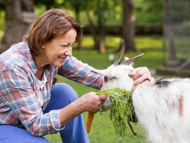 Side view woman feeding a goat with carrots