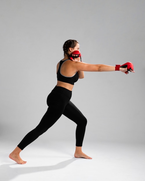 Side view woman in fitness clothes punching with box gloves