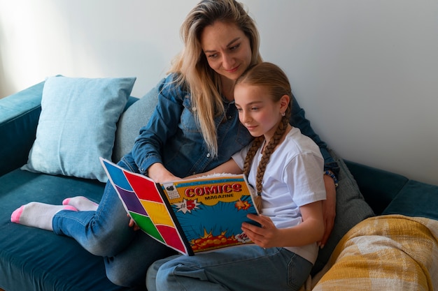 Free photo side view woman and girl reading comics indoors