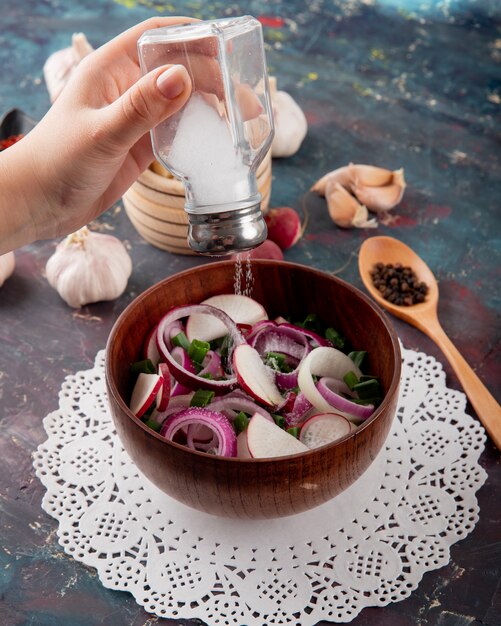 Side view of woman hand adding salt to vegetable salad on green and maroon background