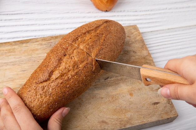 Side view of woman hands cutting baguette with knife on wooden surface and background