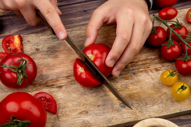 Side view of woman hands cutting tomato on cutting board with knife on wooden surface
