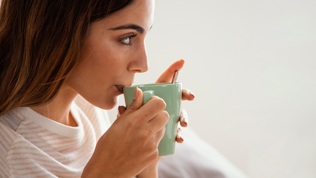 コピースペースとベッドでコーヒーを飲んでいる女性の側面図