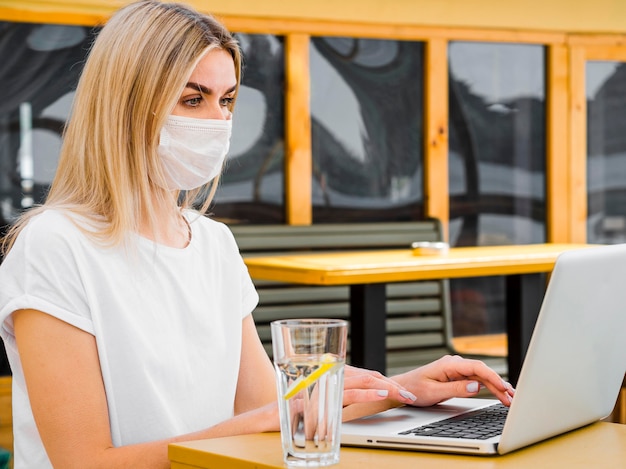 Vista laterale della donna che ha bicchiere d'acqua e che lavora al computer portatile