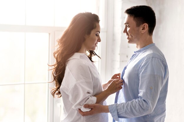 Side view of woman helping man buttoning his shirt