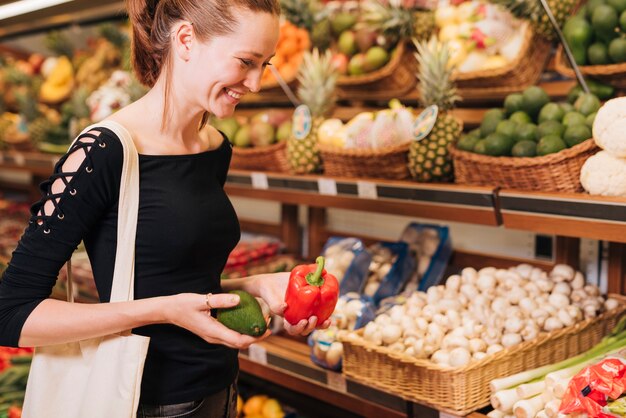 side view woman holding avocado and bell pepper