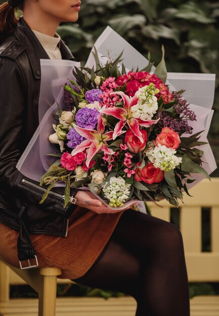 ピンク色のバラと白い色のキンギョソウの花ピンクのアジサイ紫カーネーションとトルコギキョウのユリの花束を保持している女性の側面図