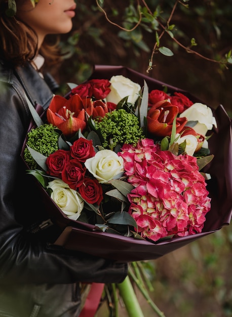 Side view of a woman holding a bouquet of white and red color roses with red color tulips pink color hydrangea and trachelium wall flowers