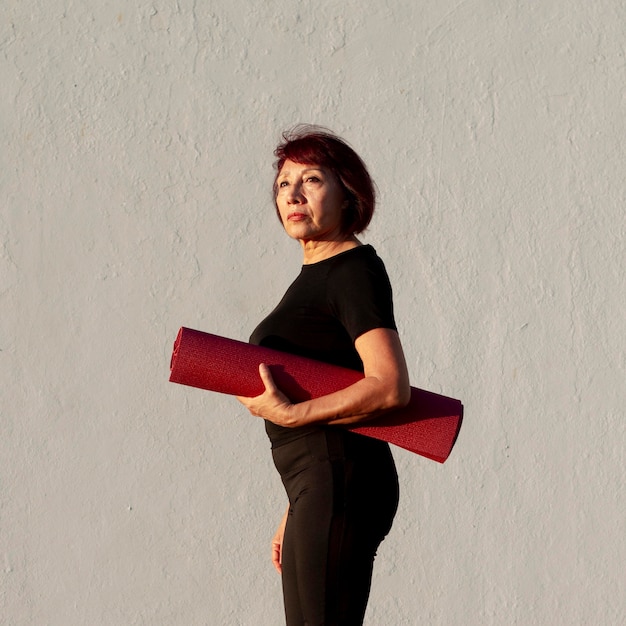 Free photo side view woman holding a fitness mat