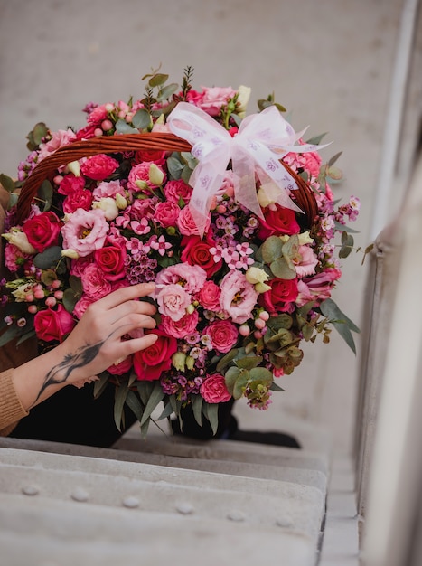 Side view of a woman holding a flower composition with pink roses eustoma and eucalyptus in a wicker basket