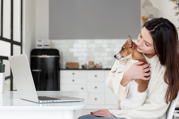 Side view of woman holding her dog while looking at laptop