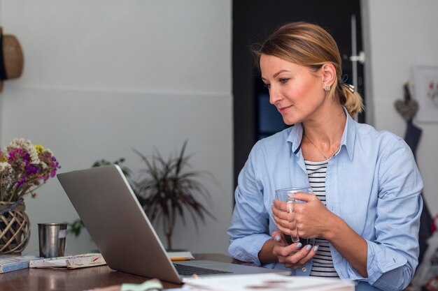 Free photo side view of woman holding mug and looking at laptop