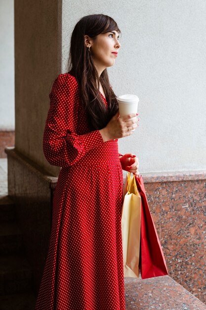 Side view of woman holding shopping bags and coffee