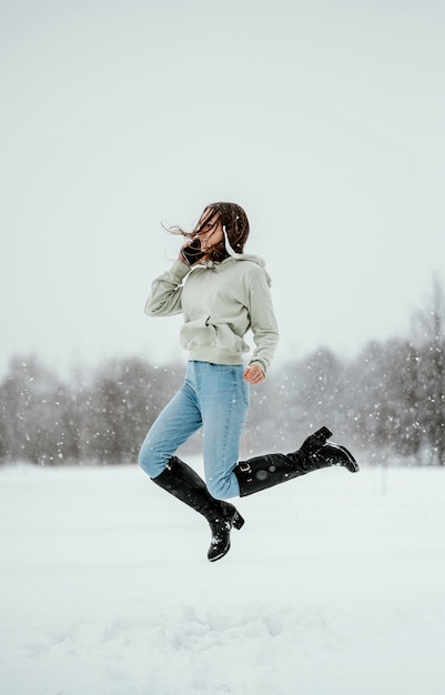 Side view of woman holding smartphone and jumping in the air outdoors