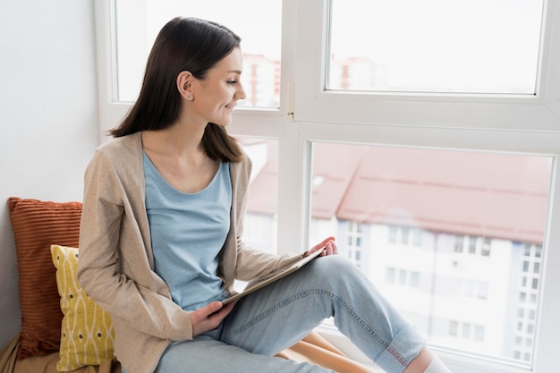 Free photo side view of woman holding tablet next to window