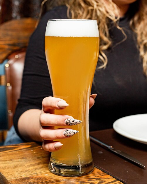 Side view of a woman holding a tall glass of light beer