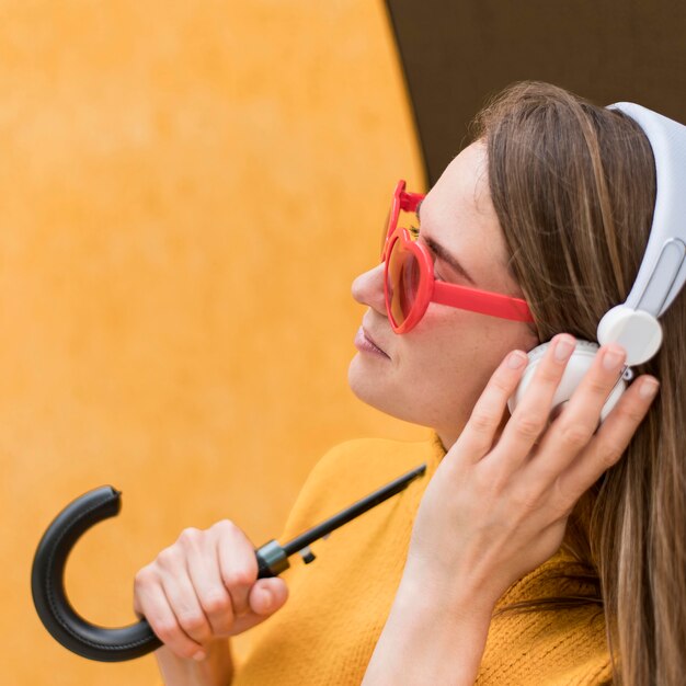 Side view woman holding an umbrella while using headphones