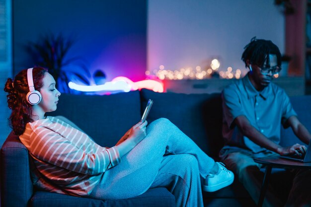 Side view of woman at home with boyfriend using tablet and headphones