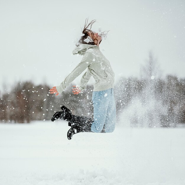 Side view of woman jumping outdoors in winter snow