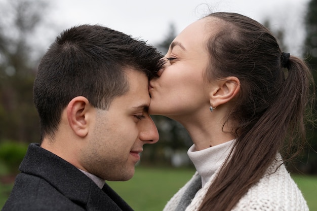 Free photo side view woman kissing man's forehead