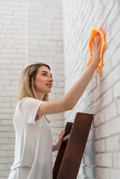 Side view of woman on a ladder cleaning brick wall