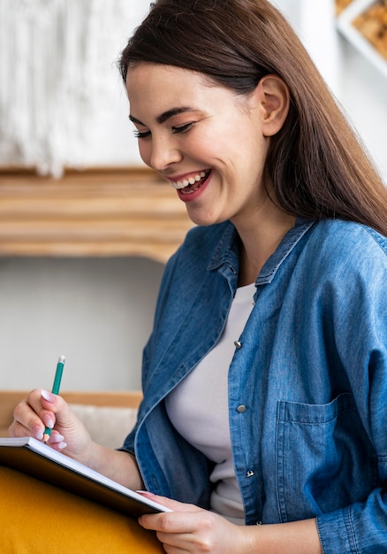 Side view of woman laughing while writing diary