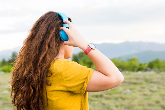 自然の中でヘッドフォンで音楽を聴く女性の側面図