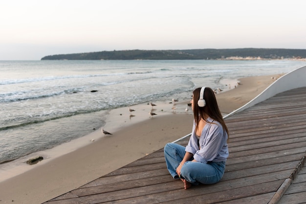 Free photo side view woman listening to music next to the sea