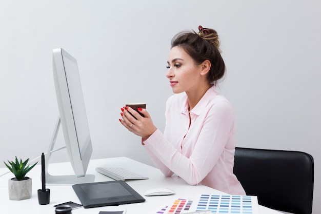 Side view of woman looking at computer while holding cup of coffee