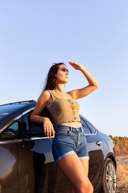 Side view of woman looking towards the sun while resting on car