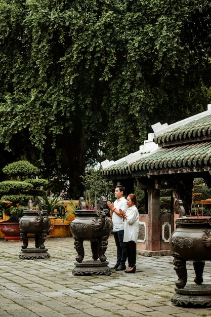 Free photo side view of woman and man praying at the temple with burning incense