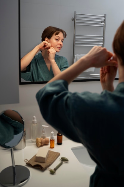 Free photo side view woman massaging face in bathroom