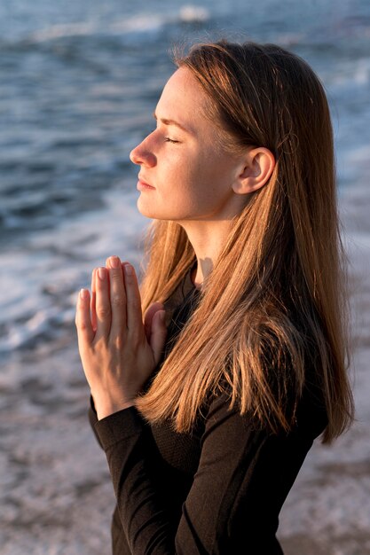 Free photo side view woman meditating on the beach