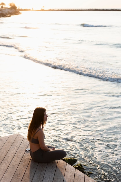 Вид сбоку женщина медитирует рядом с морем