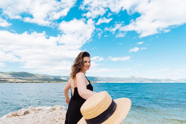 Side view of woman at the ocean holding hat