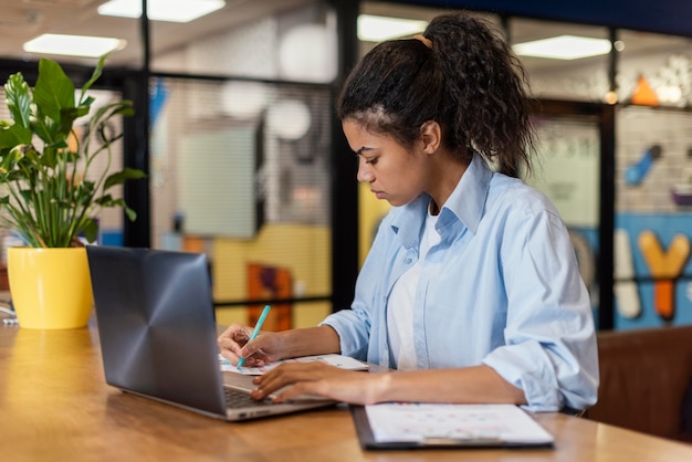 Вид сбоку женщины в офисе, работающей с ноутбуком